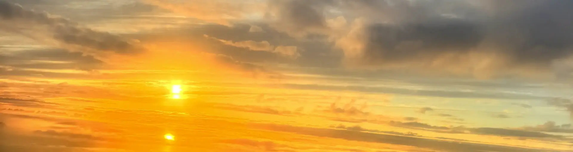 Golden sunset over a calm ocean, with orange and yellow hues reflecting on the water and scattered clouds above.
