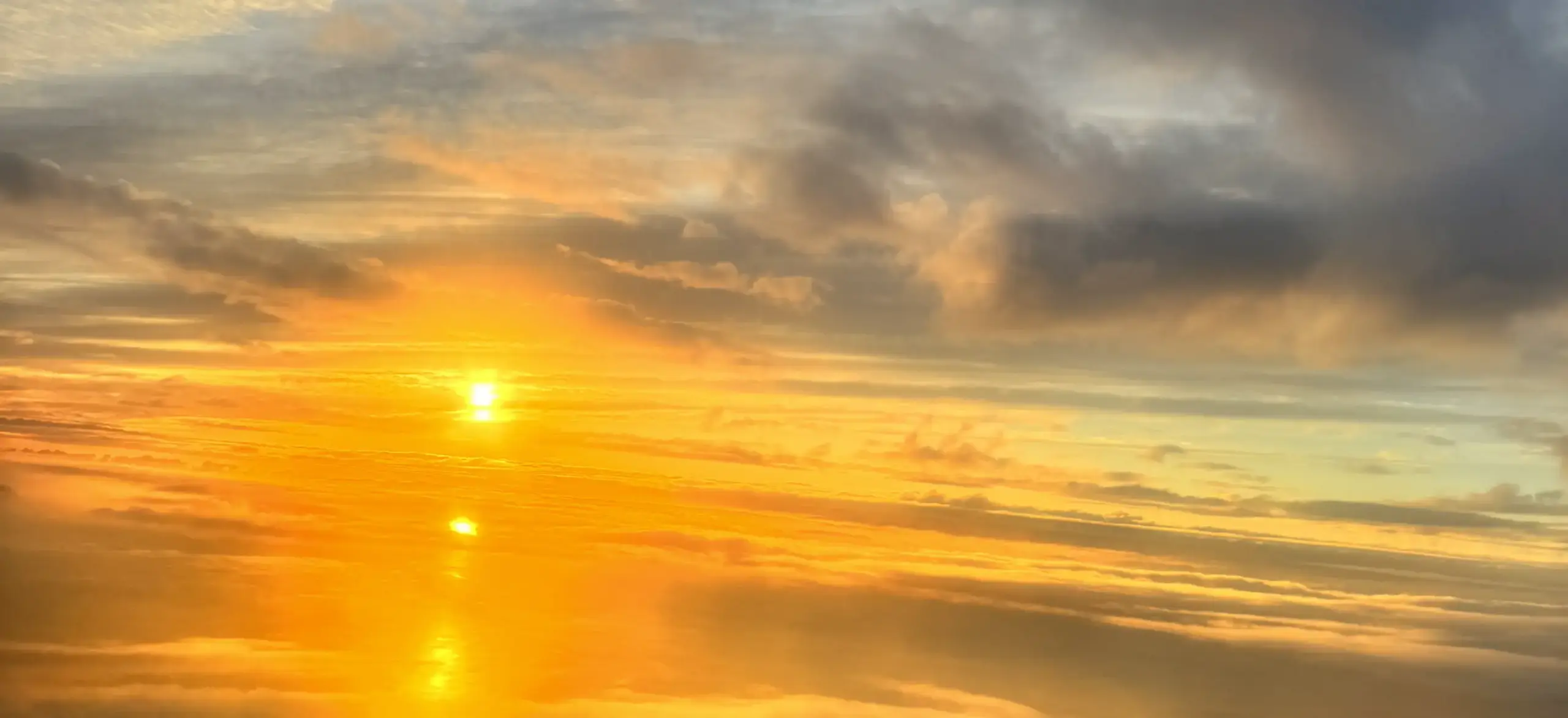 Golden sunset over a calm ocean, with orange and yellow hues reflecting on the water and scattered clouds above.