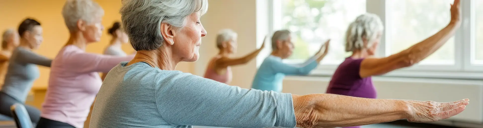Older adults in a bright studio performing arm stretches while seated on chairs, arms extended forward.